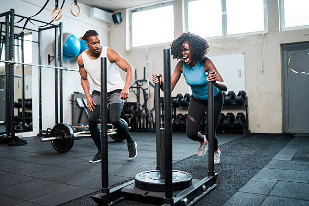 Determined athlete pushing a weighted sled with a trainer supporting